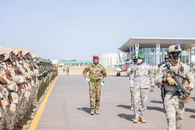 Le général Assimi Goïta, président de la Transition au Mali, en uniforme militaire vert, passe en revue des troupes lors d'un événement officiel.