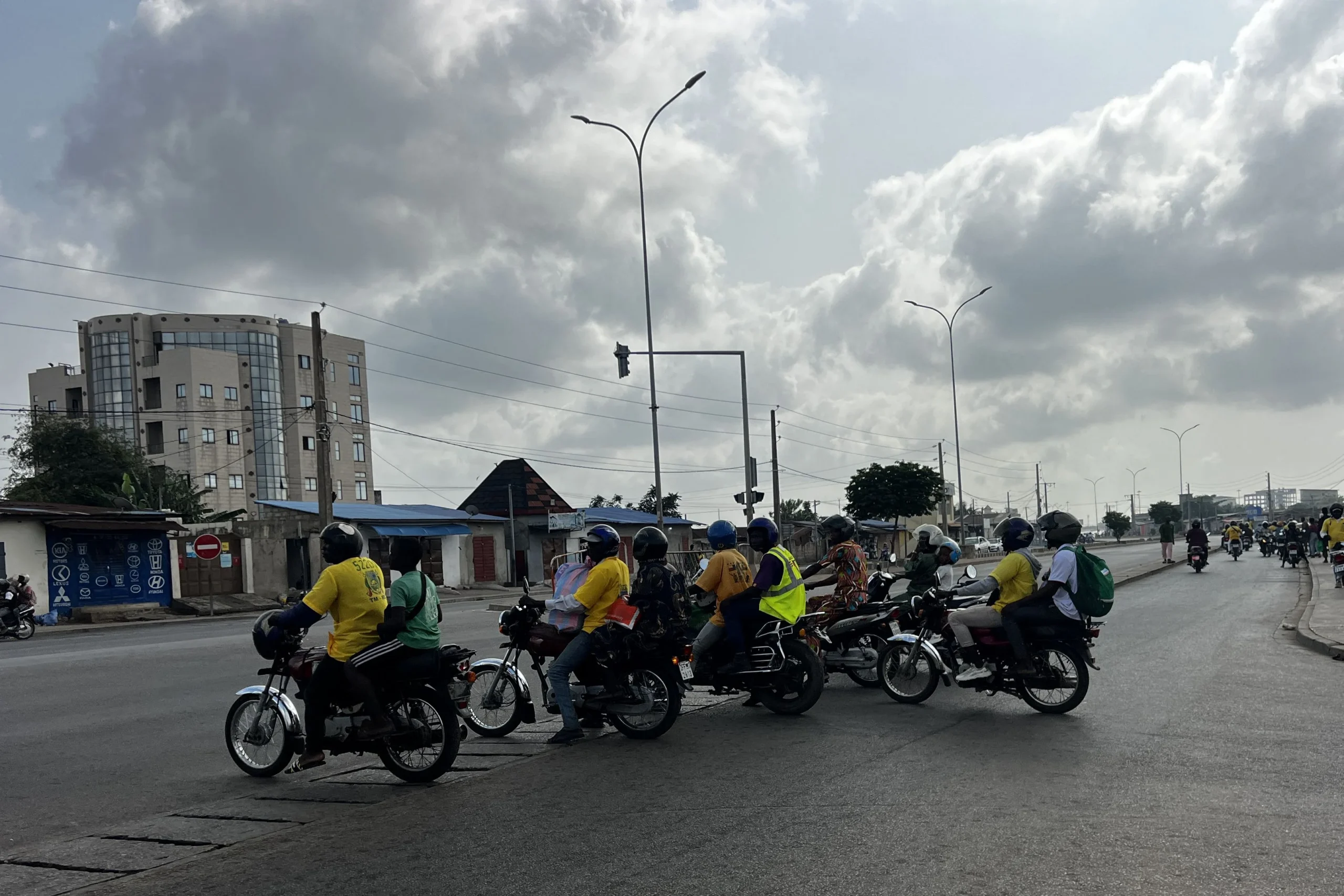 Motos-taxis transportant des passagers à un carrefour de Cotonou, avec des rumeurs de coup d’État en arrière-plan