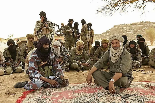 Combattants touaregs en discussion sous un arbre dans un campement désertique